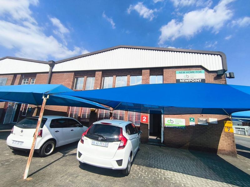 Front exterior view of an industrial unit featuring a brick facade, corrugated metal roof, and a dedicated shade cloth carport area.