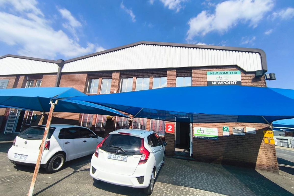 Front exterior view of an industrial unit featuring a brick facade, corrugated metal roof, and a dedicated shade cloth carport area.