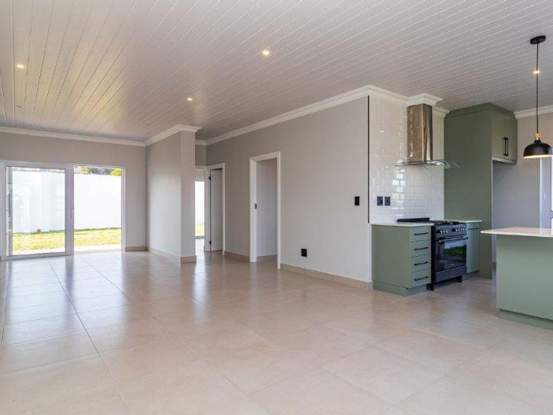 Spacious open-plan living and kitchen area featuring modern cabinetry, a gas stove, tiled floors, and sliding doors leading to the garden.