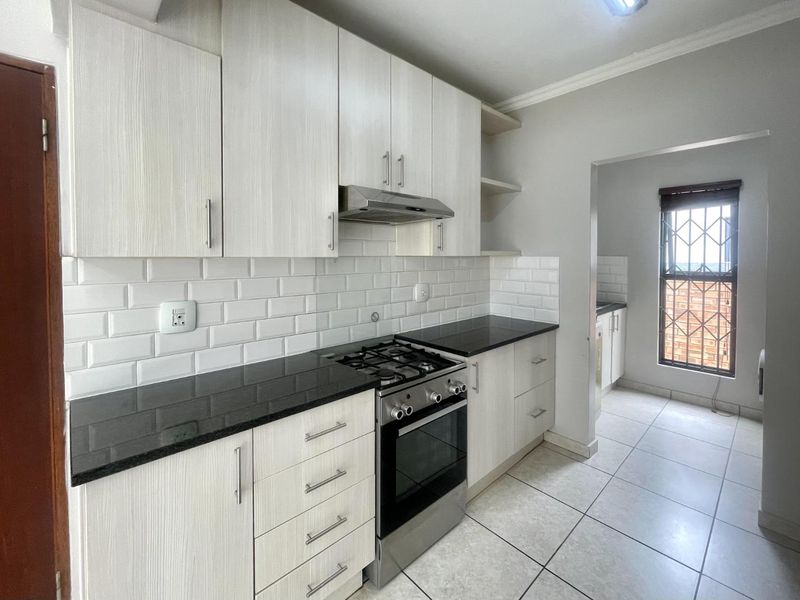 Modern kitchen featuring light wood-grain cabinetry, granite countertops, subway tile backsplash, and a gas stove, with an adjoining scullery area.