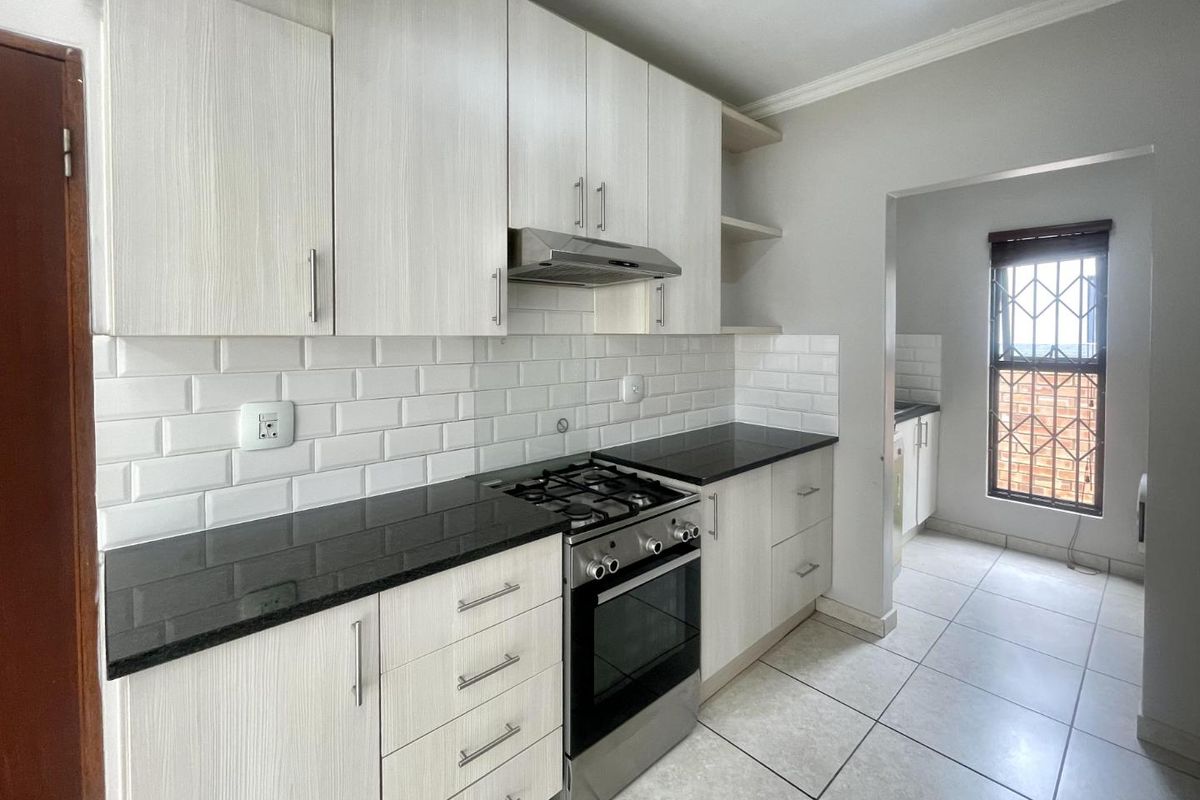 Modern kitchen featuring light wood-grain cabinetry, granite countertops, subway tile backsplash, and a gas stove, with an adjoining scullery area.
