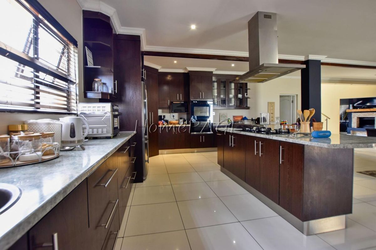 Modern kitchen featuring dark wood cabinetry, granite countertops, a central island with a gas hob, and a stainless steel extractor fan.