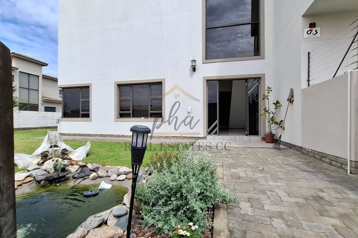 Rear exterior view of the house featuring a paved patio area, a small garden pond, and large windows.