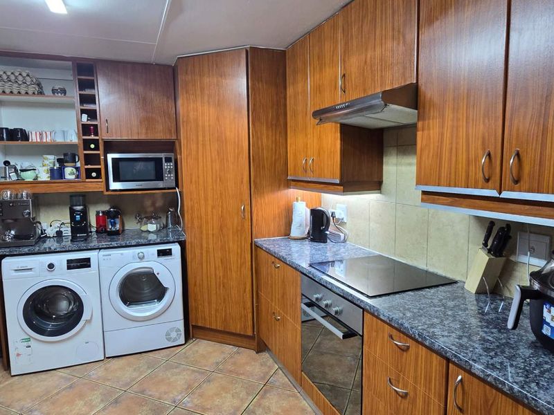 A functional kitchen featuring wood-finish cabinetry, granite countertops, integrated appliances including an oven and hob, and tiled flooring with a neutral backsplash.