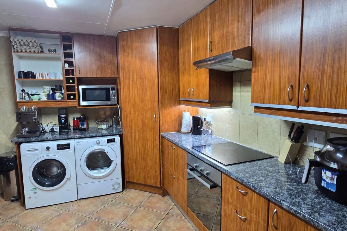 A functional kitchen featuring wood-finish cabinetry, granite countertops, integrated appliances including an oven and hob, and tiled flooring with a neutral backsplash.