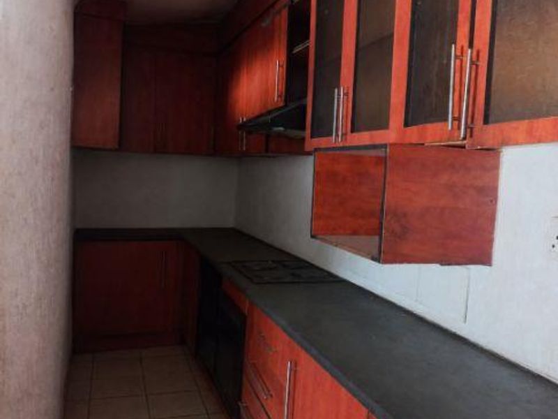 A galley-style kitchen featuring wood-look cabinetry, dark countertops, and built-in appliances, currently requiring maintenance and cosmetic updates.