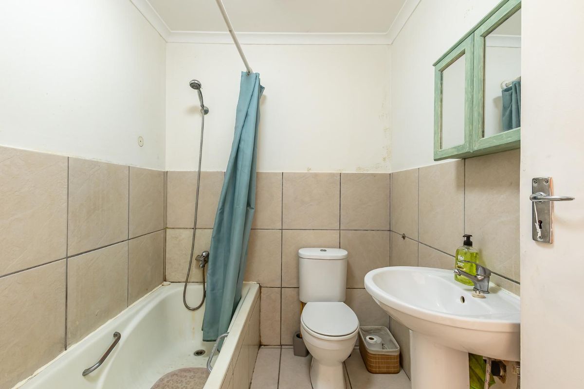 A functional bathroom featuring a bathtub with shower attachment, pedestal basin, and toilet, with visible signs of wear and wall staining.