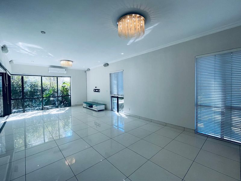 Spacious, light-filled living area featuring polished porcelain floor tiles, modern ceiling light fixtures, and large sliding doors opening to a garden view.
