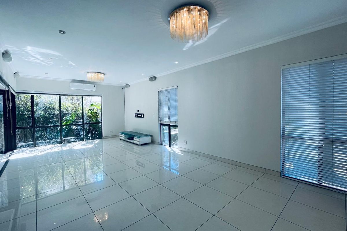 Spacious, light-filled living area featuring polished porcelain floor tiles, modern ceiling light fixtures, and large sliding doors opening to a garden view.