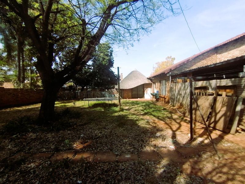 Rear garden area featuring a brick exterior, thatched roof structure, and mature trees, offering potential for landscaping and outdoor improvement.
