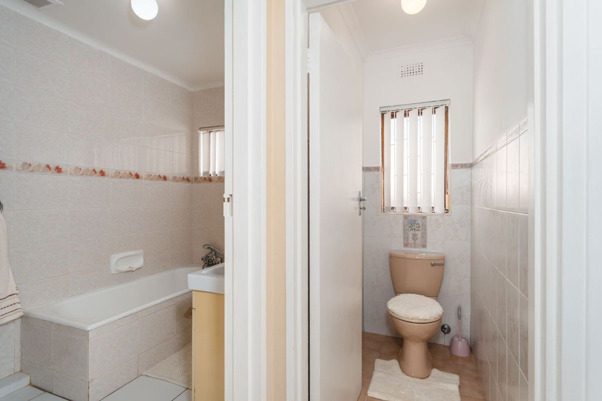 A split-layout bathroom featuring a separate bathtub and basin area alongside a private toilet room with dated fixtures and neutral wall tiling.