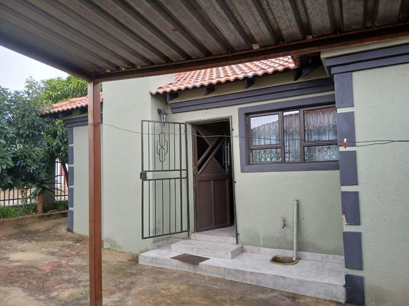 Exterior view of the house entrance featuring a covered patio area, security gate, tiled step, and terracotta roof tiles.