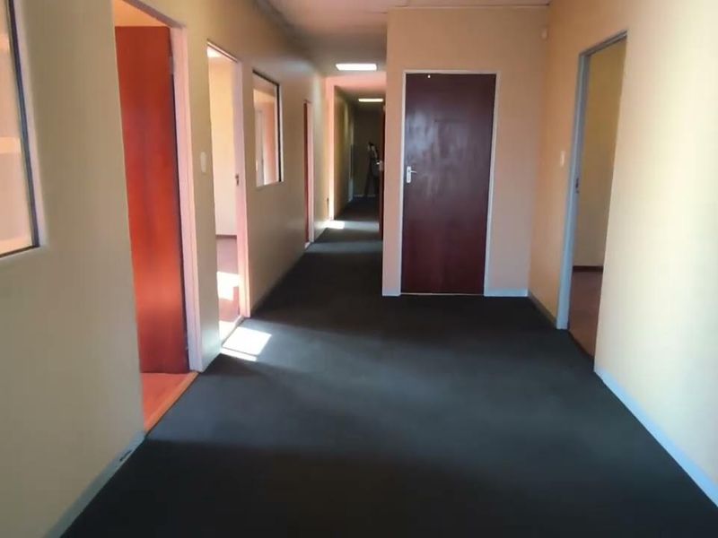 A long office hallway featuring neutral wall finishes, carpeted flooring, and multiple access points to individual office rooms.