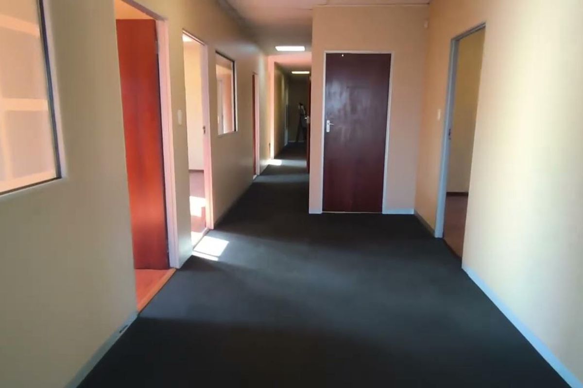 A long office hallway featuring neutral wall finishes, carpeted flooring, and multiple access points to individual office rooms.