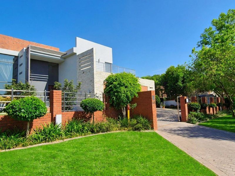 A modern architectural home featuring a brick and stone facade, glass elements, a paved driveway, and a well-maintained landscaped front garden.