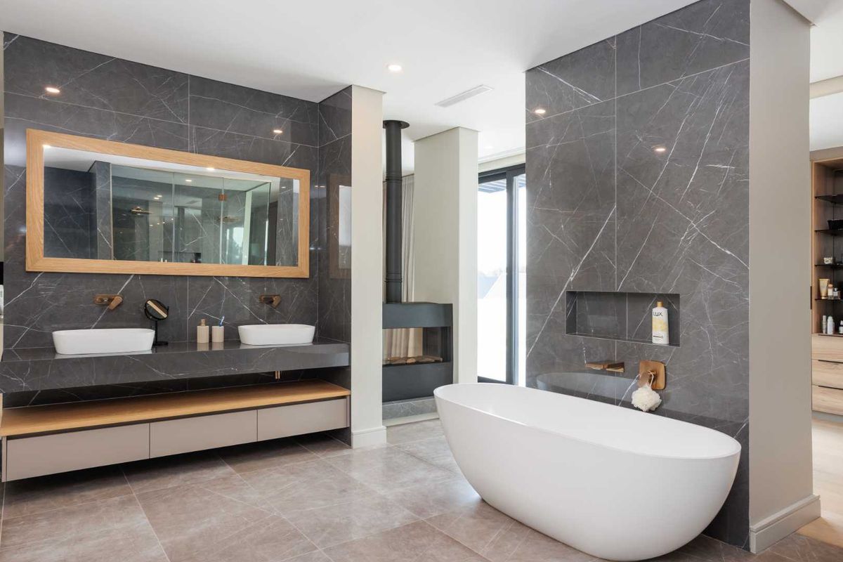 Modern luxury bathroom featuring a double vanity, freestanding bathtub, stone wall finishes, and a built-in fireplace for a sophisticated spa-like atmosphere.