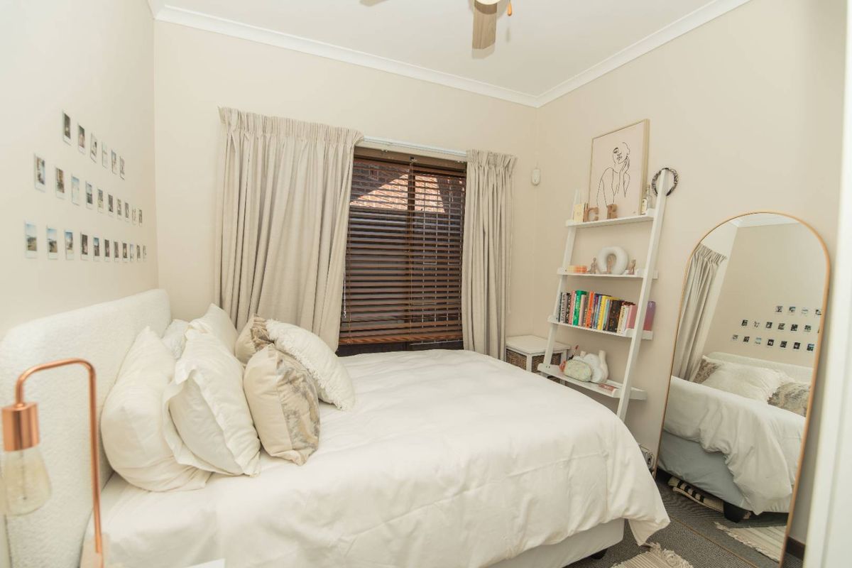 A cozy bedroom featuring neutral walls, a ceiling fan, and window treatments including venetian blinds and curtains.