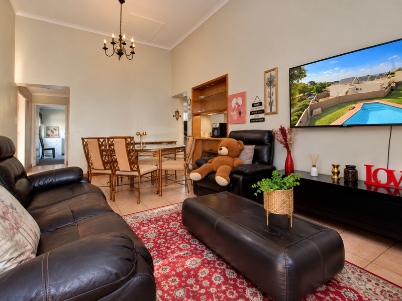 Spacious open-plan living and dining area featuring tiled flooring, built-in display shelving, and a high coved ceiling with a classic chandelier.