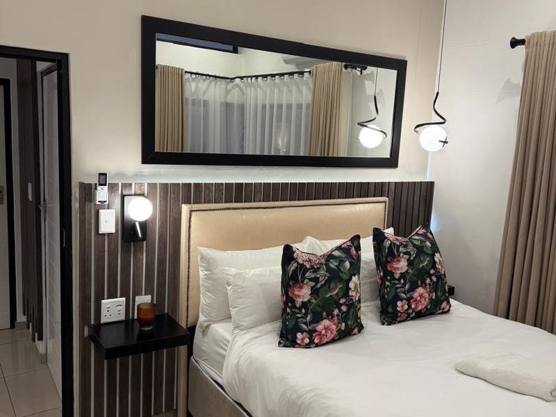 A well-maintained bedroom featuring a modern built-in headboard with integrated lighting, tiled floors, and a large decorative wall mirror.