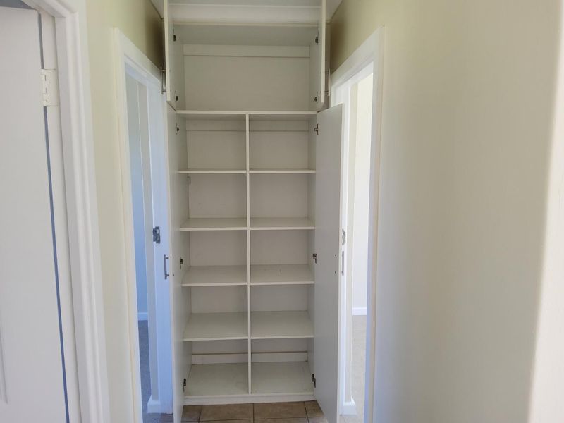 A functional hallway featuring a tall, white built-in linen cupboard with multiple storage shelves.