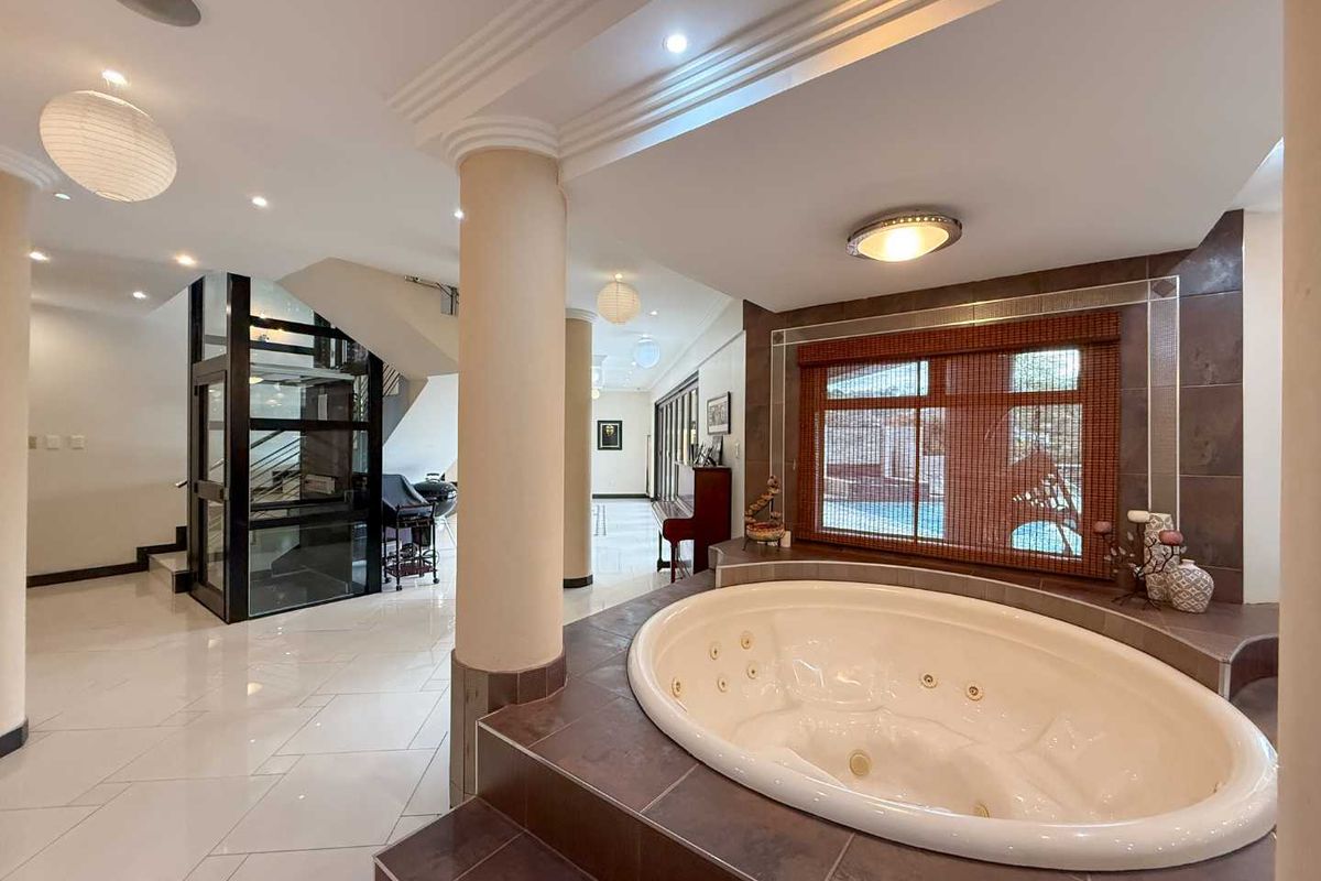 Spacious interior area featuring a built-in jetted spa bath, tiled flooring, recessed ceiling lighting, and a modern glass-enclosed elevator.