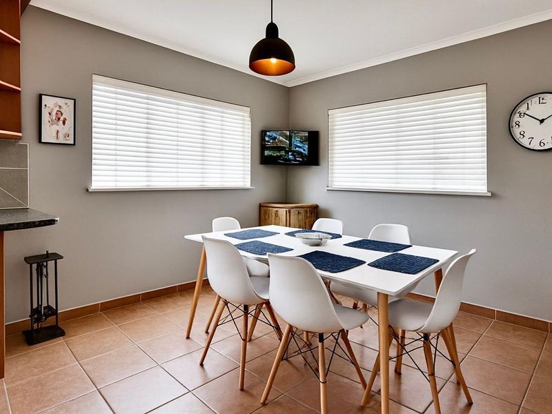 A well-maintained dining area featuring tiled flooring, neutral wall tones, venetian blinds, and modern pendant lighting, creating a bright and functional space.