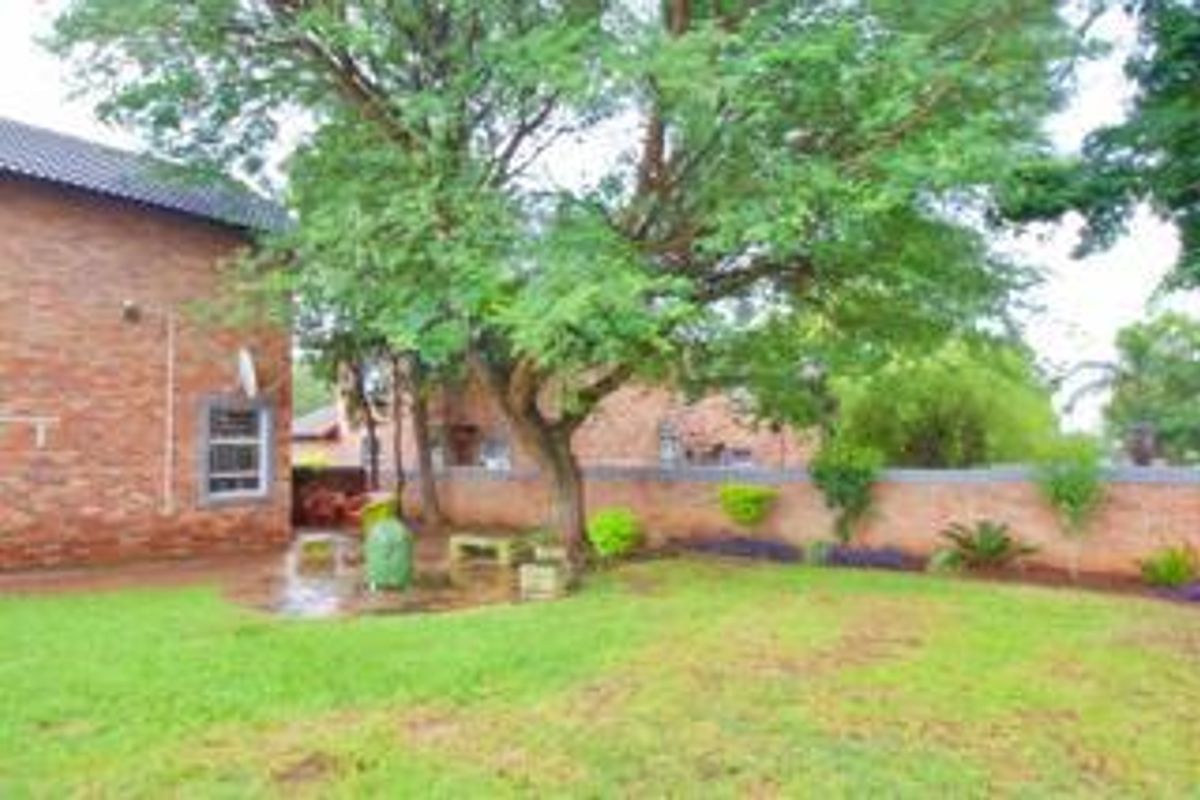 A private rear garden featuring a paved patio area, mature tree, and brick boundary wall, adjacent to the townhouse's exposed brick exterior.