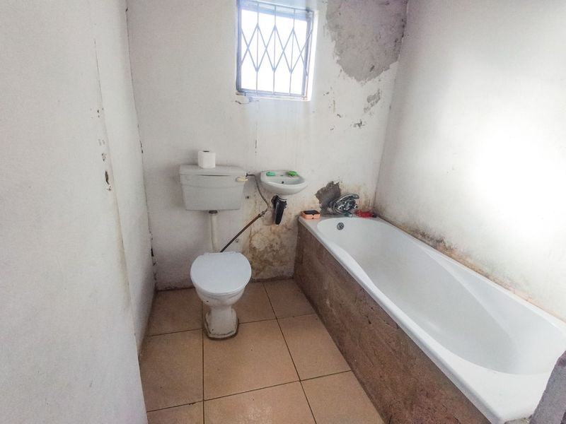 A small bathroom featuring a bathtub, toilet, and wall-mounted basin, currently requiring significant renovation and wall repairs.