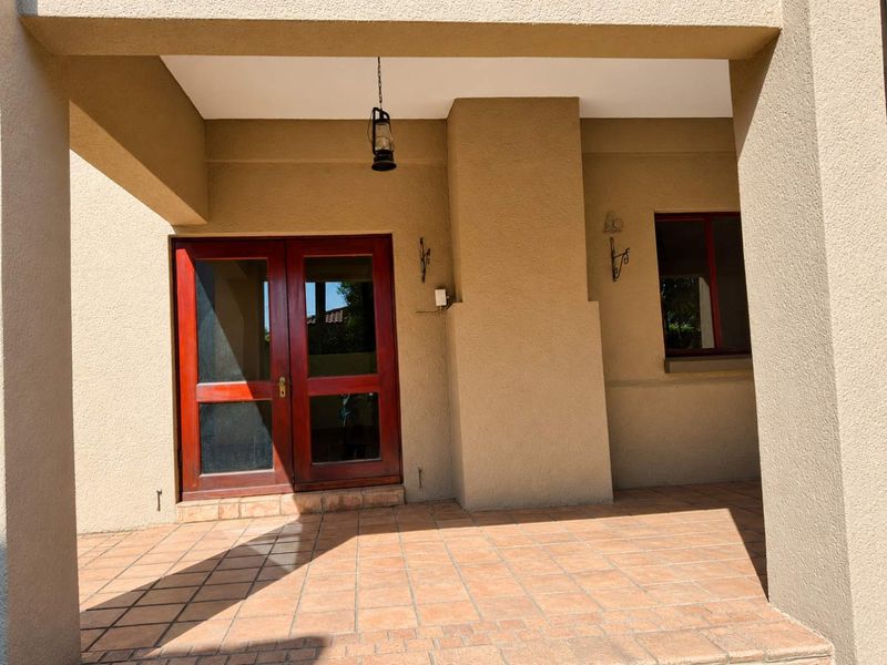 A covered patio area featuring terracotta floor tiles and double timber doors, providing a sheltered outdoor transition space.
