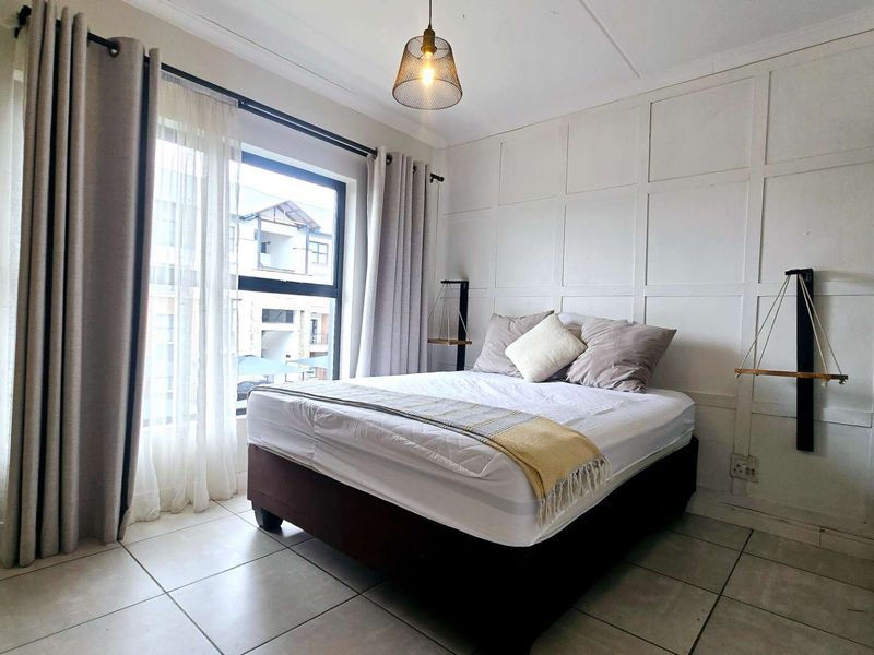 A well-lit bedroom featuring decorative wall paneling, neutral tiled flooring, and a large window providing natural light.