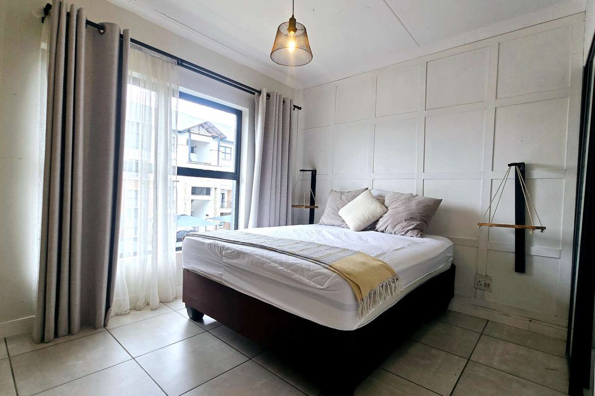 A well-lit bedroom featuring decorative wall paneling, neutral tiled flooring, and a large window providing natural light.