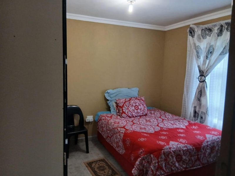 A compact bedroom featuring neutral wall tones, tiled flooring, and a window with curtain fixtures.