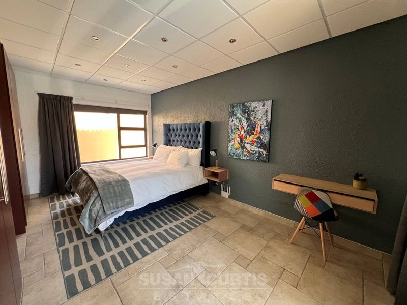 A spacious bedroom featuring tiled flooring, a suspended ceiling with recessed lighting, and a built-in wall-mounted desk.