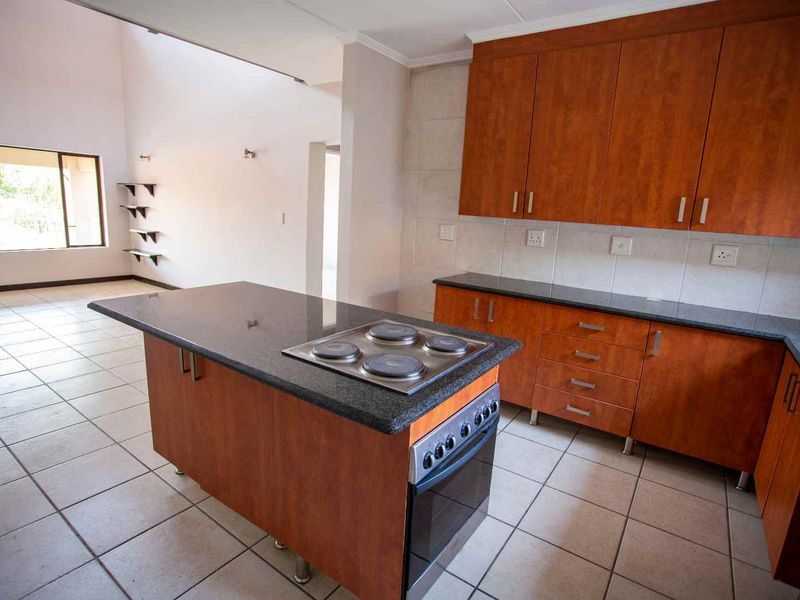 Open plan kitchen and living area featuring wooden cabinetry, granite countertops, built-in oven and hob, and tiled flooring throughout.