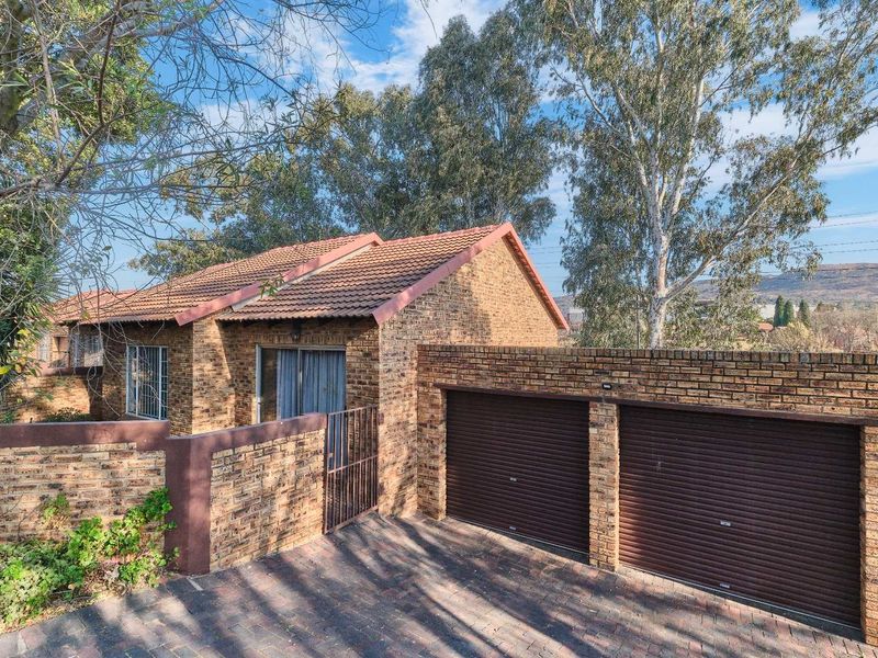 Front exterior view of a face brick townhouse featuring a double garage with roller shutter doors and a paved driveway.