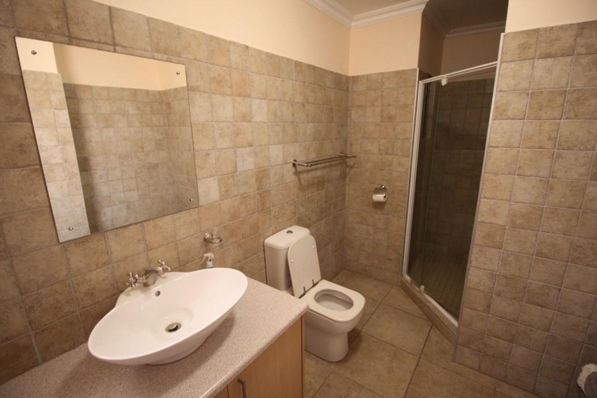 A functional bathroom featuring a vanity with a vessel sink, a toilet, and a glass-enclosed shower with neutral wall and floor tiling.