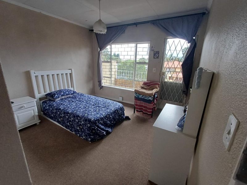 A bedroom featuring carpeted flooring, security gate access, and burglar bars on the window, offering a functional space in need of cosmetic updates.