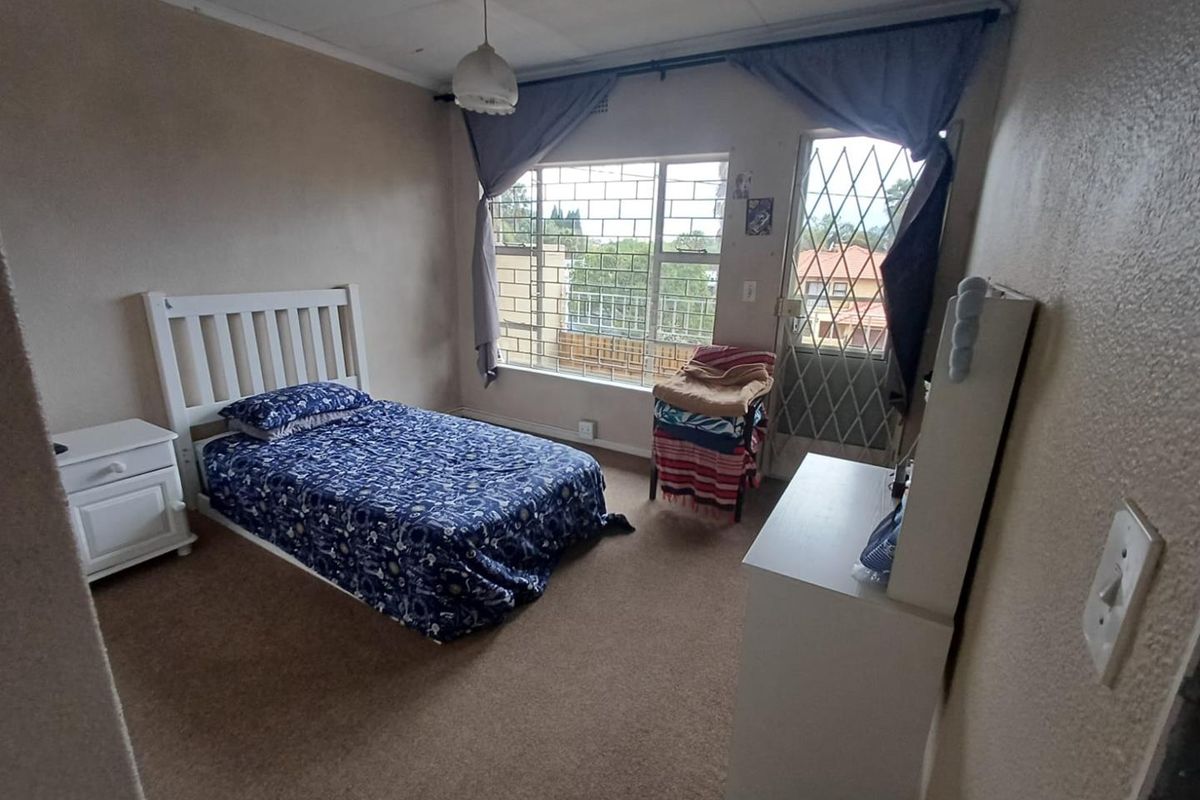 A bedroom featuring carpeted flooring, security gate access, and burglar bars on the window, offering a functional space in need of cosmetic updates.
