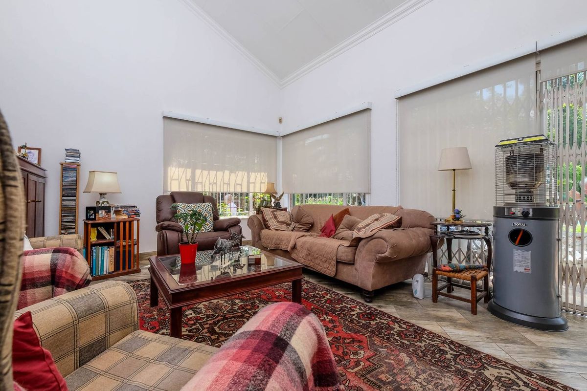 Spacious living room featuring a high vaulted ceiling, large windows with roller blinds, and durable tiled flooring.