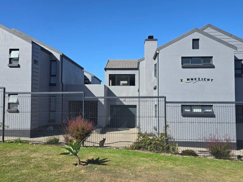 Front elevation of the Zonnezicht apartment complex featuring modern grey facade, secure mesh fencing, and paved driveway access.