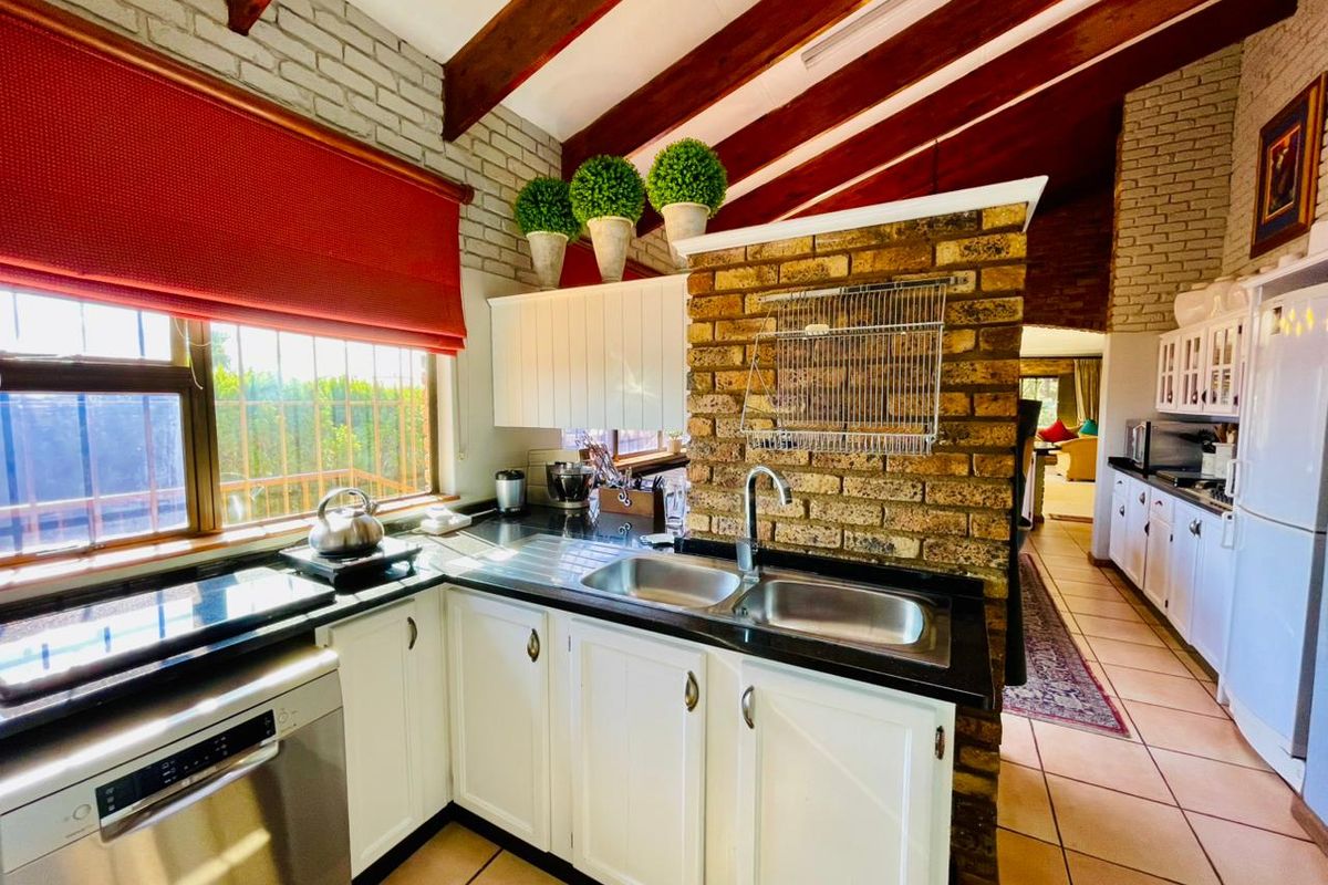 A characterful kitchen featuring exposed timber beams, a rustic brick feature wall, white cabinetry, and black granite countertops with a double sink.