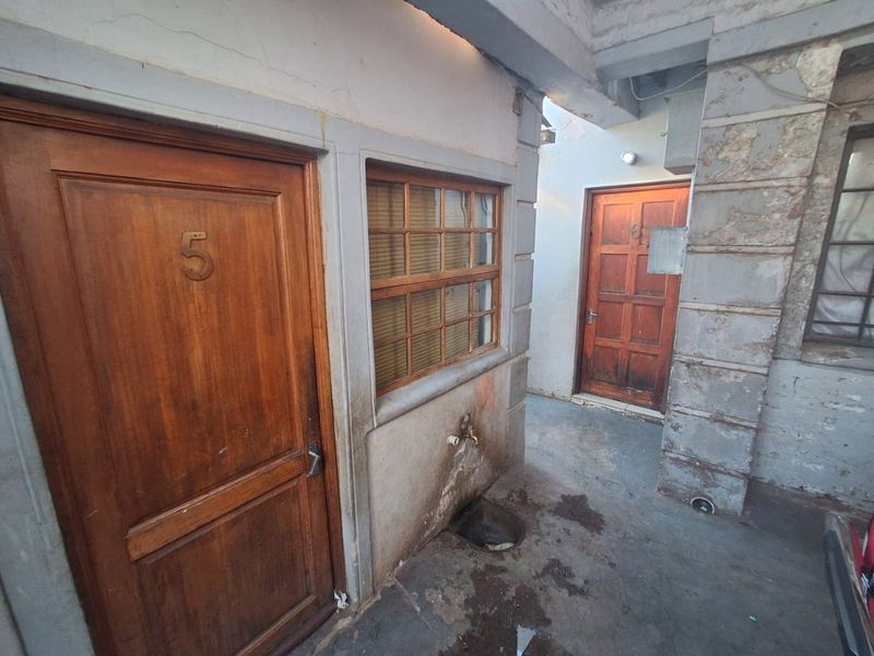 Exterior view of a rear courtyard area featuring timber doors, a window, and an external water tap, showing significant signs of wear and weathering.