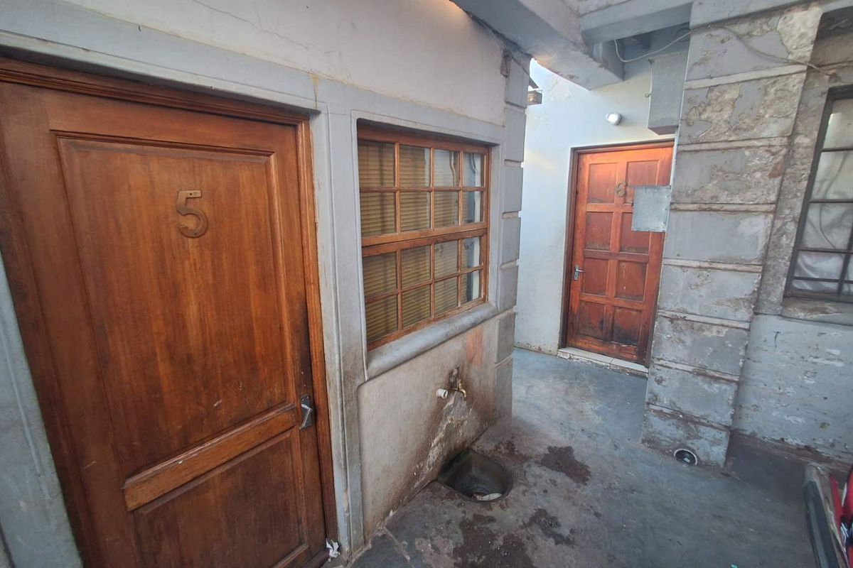 Exterior view of a rear courtyard area featuring timber doors, a window, and an external water tap, showing significant signs of wear and weathering.