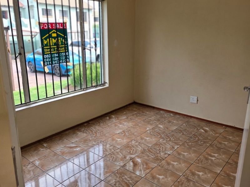 An empty bedroom featuring ceramic floor tiles, neutral wall paint, and a window fitted with security bars.