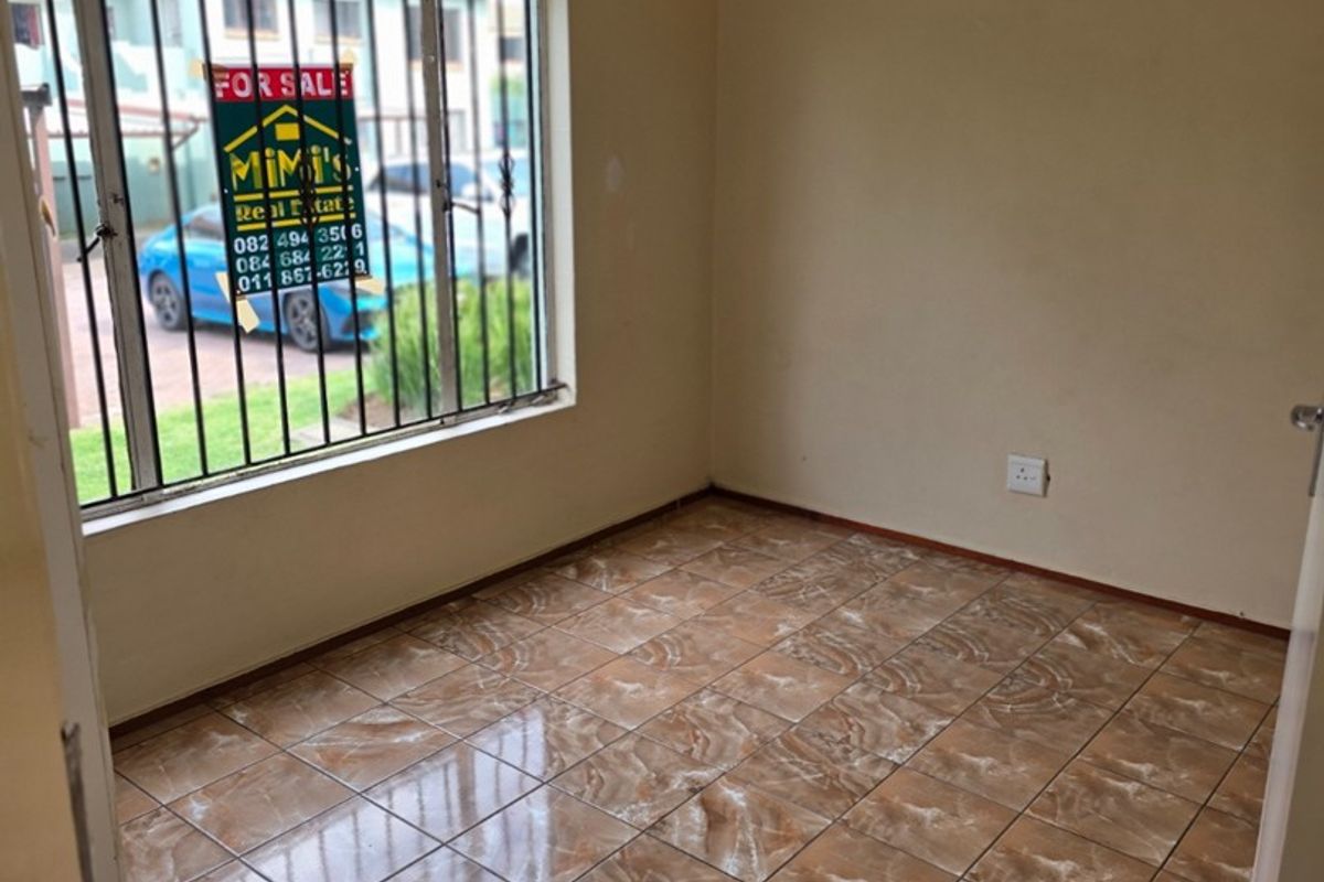An empty bedroom featuring ceramic floor tiles, neutral wall paint, and a window fitted with security bars.