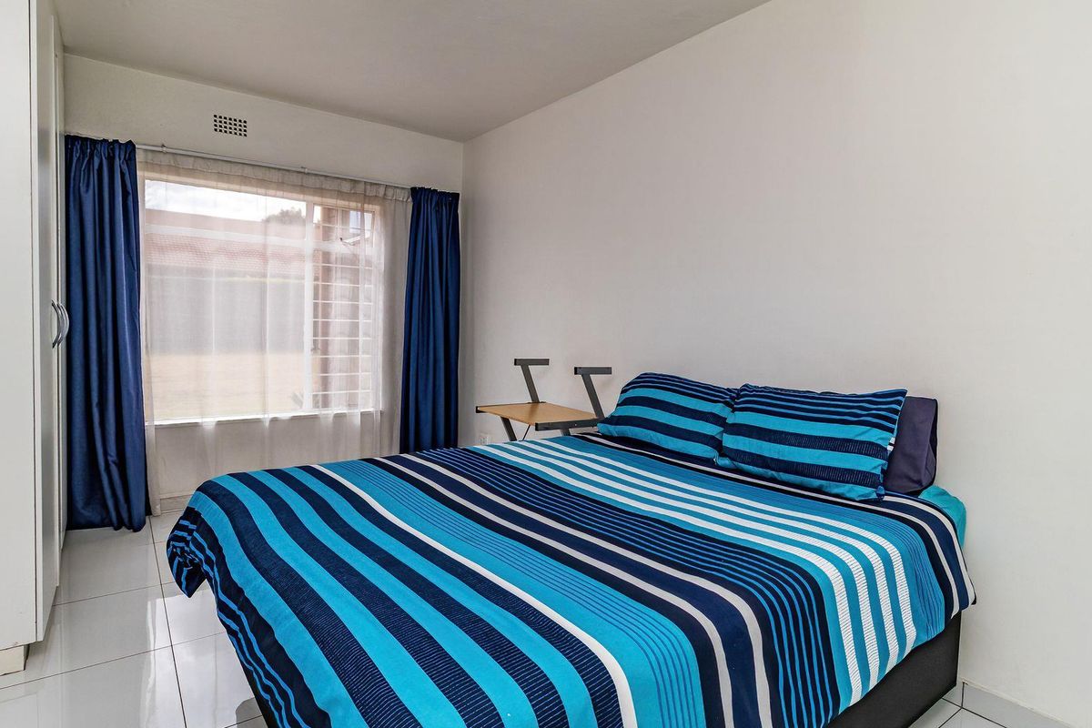 A bedroom featuring tiled flooring, a built-in wardrobe, and a window fitted with security bars.