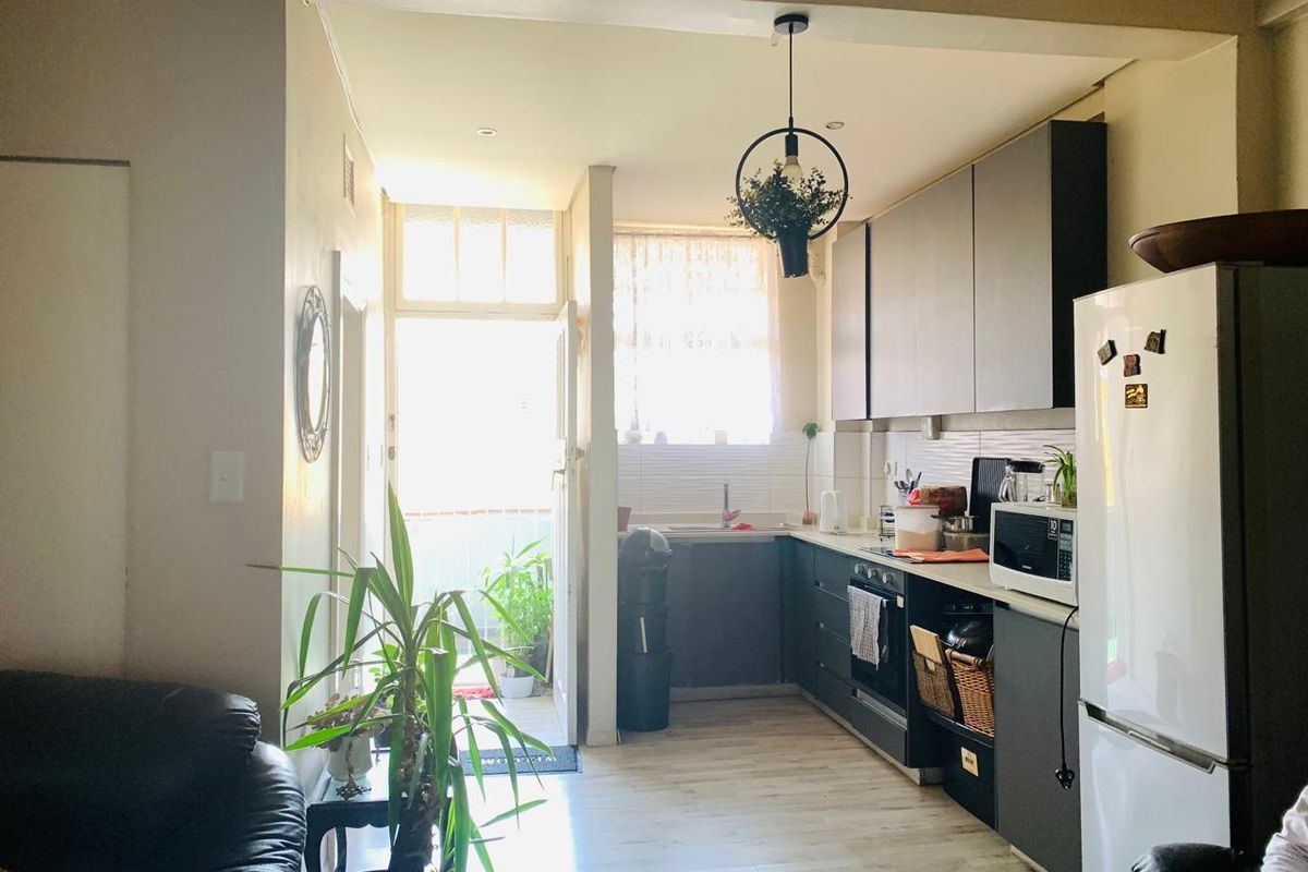 Open-plan kitchen area featuring modern dark cabinetry, laminate flooring, and direct access to an outdoor balcony space.