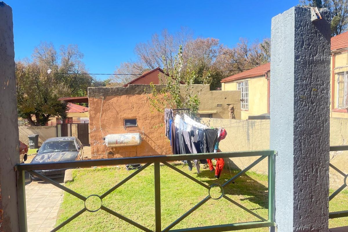 View of the rear yard area featuring a lawn, boundary wall, and exterior utility structure with a mounted geyser.