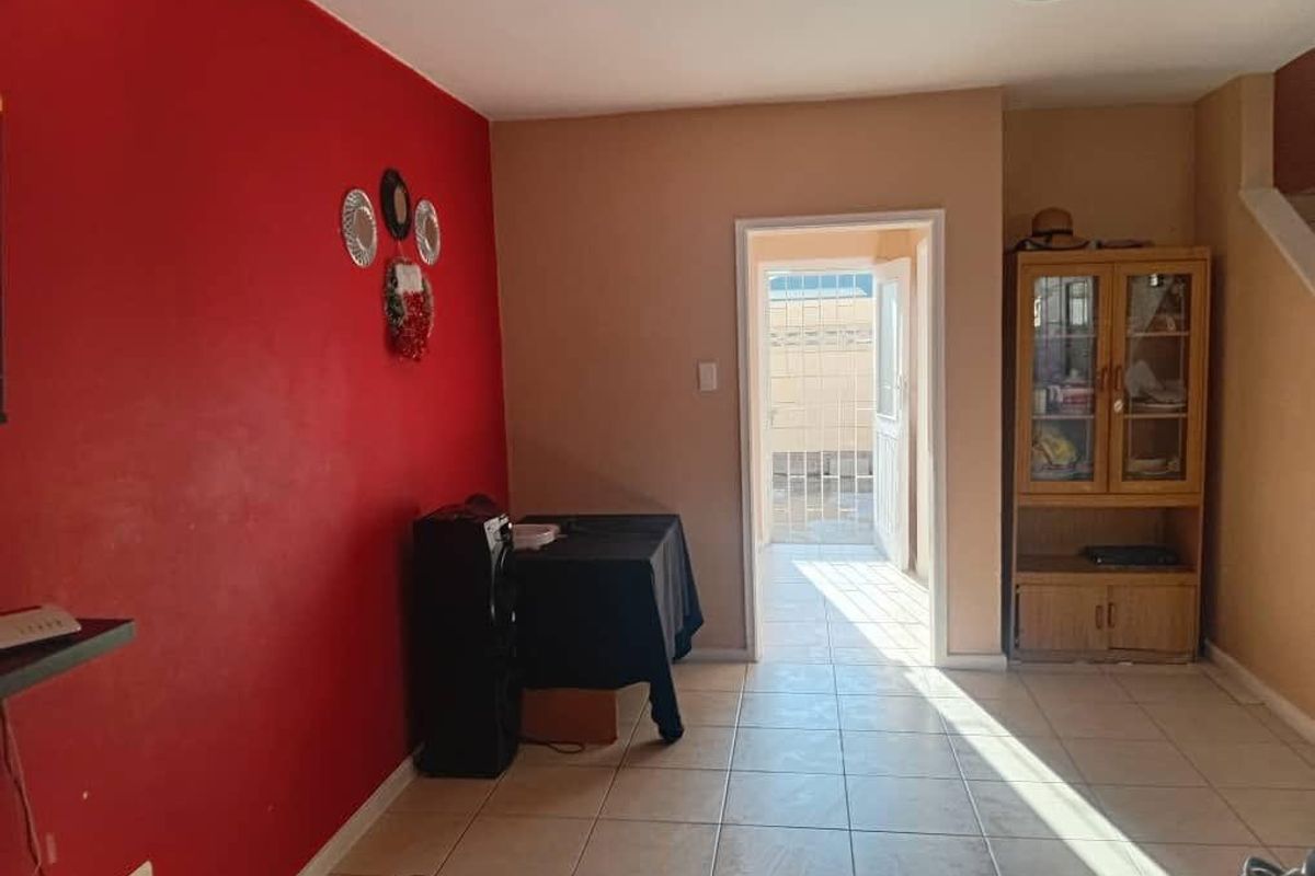 A living room area featuring tiled flooring, a bold red accent wall, and a doorway leading to an outdoor patio space.