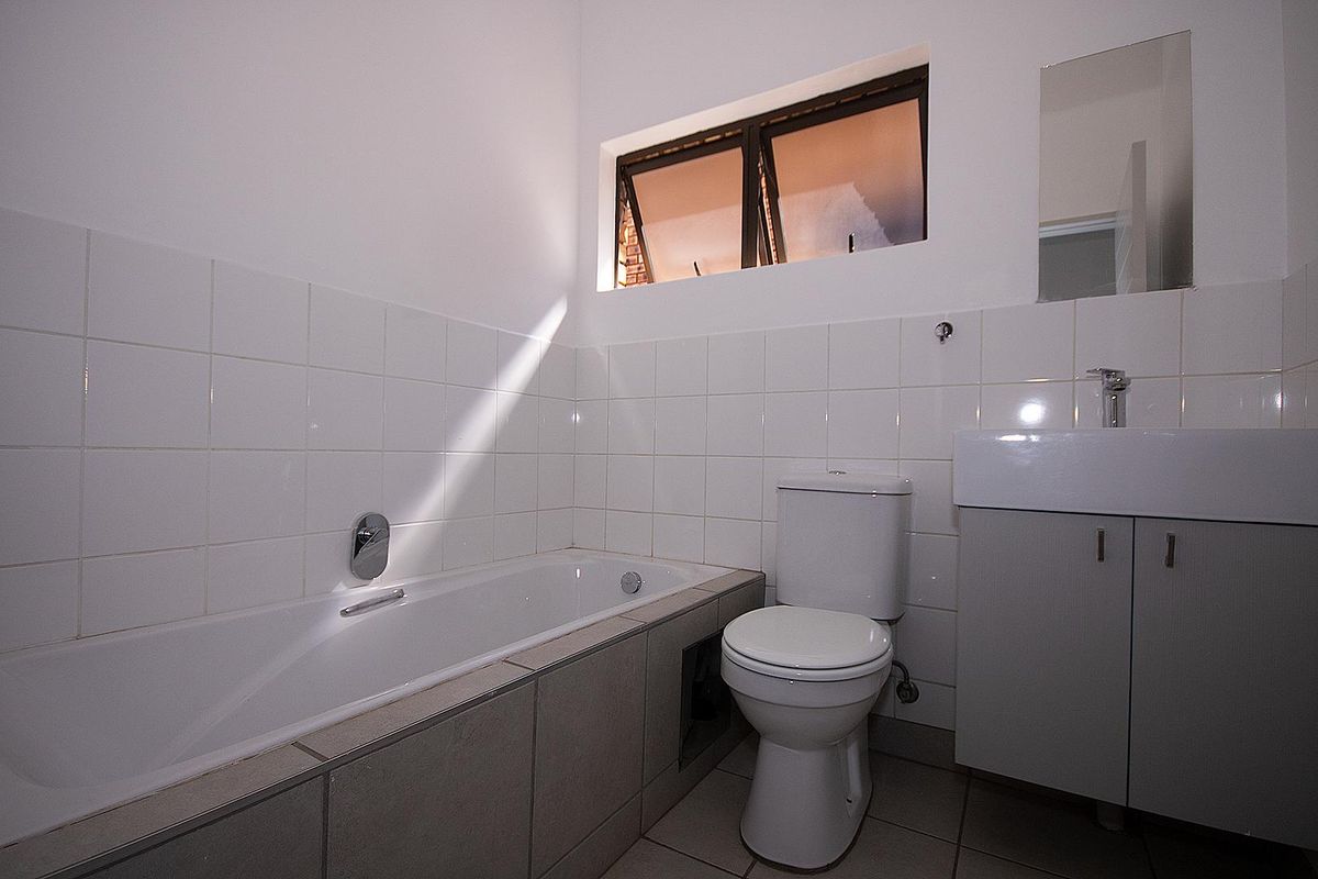 A functional bathroom featuring a built-in bathtub, a toilet, and a vanity cabinet with a washbasin, finished with neutral wall and floor tiling.